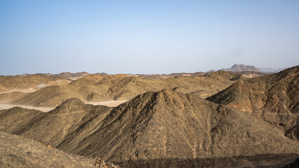 Majestic Desert Panorama: Rugged Rocky Hills, Expansive Sandy Terrain, and Clear Blue Sky, Highlighting the Stark Natural Beauty and Solitude of the Remote, Untouched Wilderness