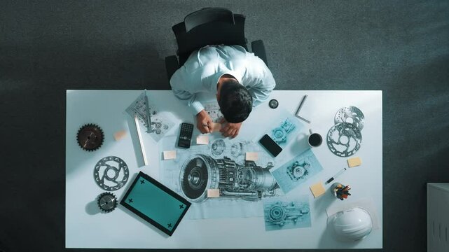 Top down view of skilled engineer writing and planning turbine engine design while sitting at meeting table with gear and electronic generator scatter around. Technician taking a note. Alimentation.