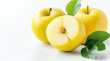 Two whole and one halved yellow apples with green leaves on white background.