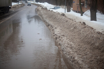 Snow is melting on the road. Puddle in spring. Highway in the water. Melting snow on the highway in the city.