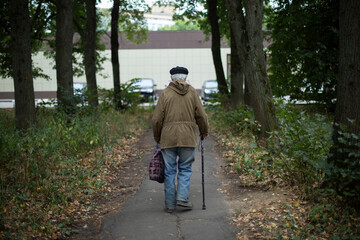 Old man walks along path in park. Poor old man walking down street. Pensioner with walking stick.