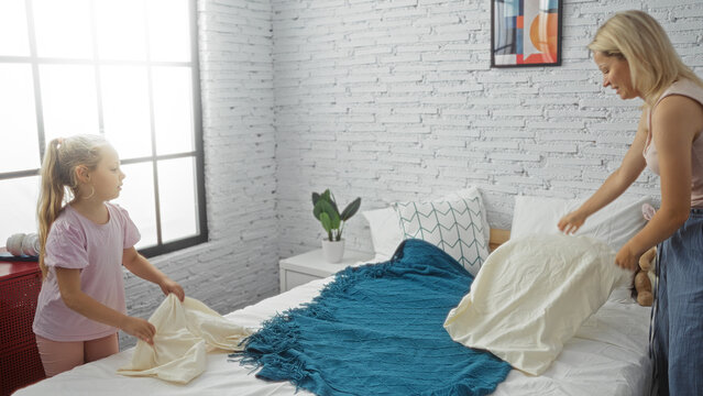 Mother and daughter making the bed together in a cozy bedroom, showcasing family bonding indoors at home. - Powered by Adobe