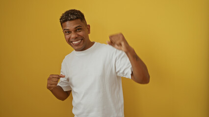 Young man in a white shirt smiles while striking a playful pose against an isolated yellow background