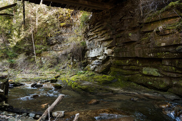 Tranquil Stream Beneath an Old Bridge Surrounded by Mossy Rocks and Lush Vegetation