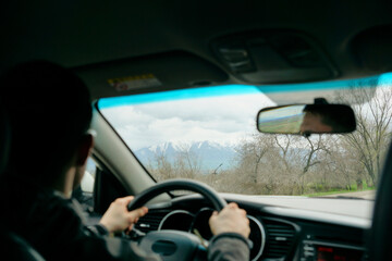 A man drives a car on a mountain road. View from inside the car from the back seat to the driver and the road