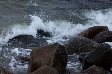 Waves with splashes and foam are beating among boulders on the shore of the North Sea