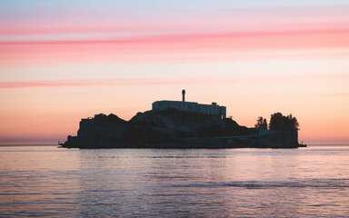 Obraz premium Island prison silhouetted against a vibrant sunset sky.