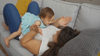 Woman playing with infant daughter on a couch in a cozy living room, showcasing maternal love and family bonding.