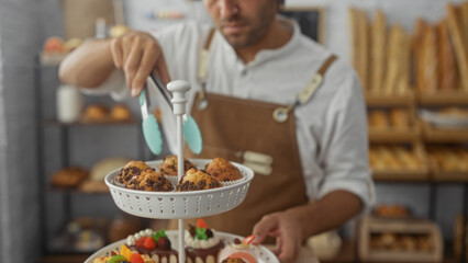 Young man working in a bakery arranging pastries with tongs displaying a variety of baked goods on...