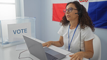 Woman working at an electoral office in the dominican republic, wearing a headset and sitting by a...