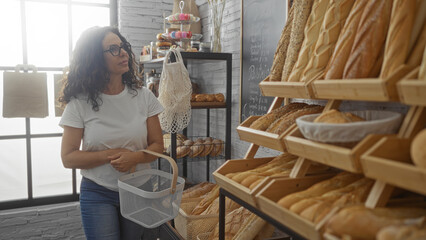 Woman shopping in a bakery with a variety of breads on display, holding a basket and looking at the...
