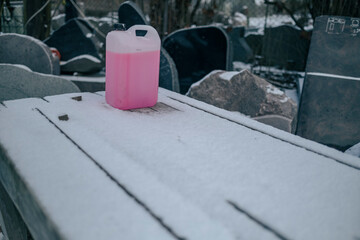 plastic can with red antifreeze liquid on snow covered table outdoors