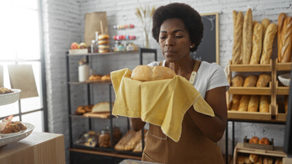 Woman inspecting fresh bread in a cozy bakery, surrounded by shelves of baked goods and a warm indoor setting, showcasing an african american female with curly hair focused on her work.