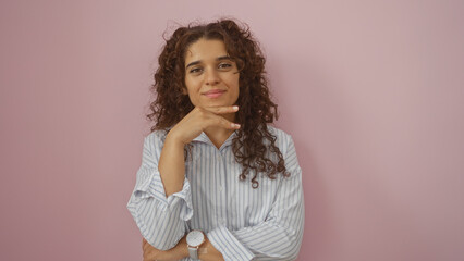 Obraz premium Young woman with brunette hair poses confidently against an isolated pink background, showcasing her natural beauty and relaxed style in a casual striped shirt