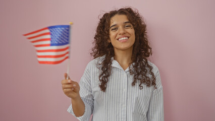 Young woman holding american flag, smiling, isolated over pink background, conveying pride and...