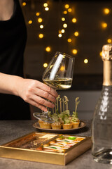 A woman holds a glass of wine in her hand in the kitchen. There is a bottle of champagne and a snack on the table. Vertical photo.
