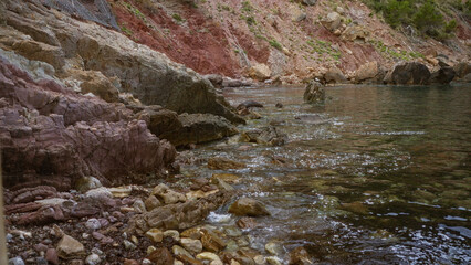 Coastal shoreline with rocky landscape and calm waters with distant hillside greenery shows rugged natural beauty and serene atmosphere