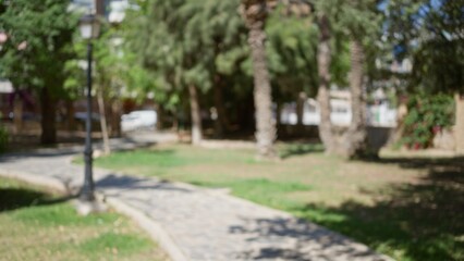 Blurred view of an outdoor park with defocused greenery, trees, and pathways illuminated by sunlight, creating an overall bokeh effect.