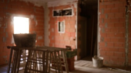 Defocused view of an unfinished construction site with brick walls, blurry tools, and building materials scattered on the floor.