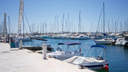 Fototapeta premium Boats docked along a sunny, blurred harbor pier with defocused masts and blue water under a clear sky