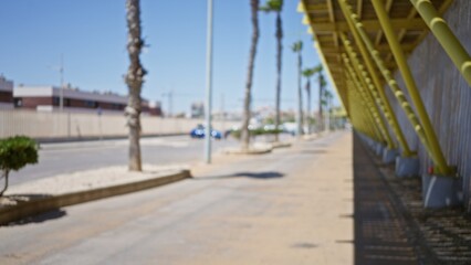 Fototapeta premium Blurry outdoor scene with a defocused road, palm trees, and distant buildings on a sunny day.