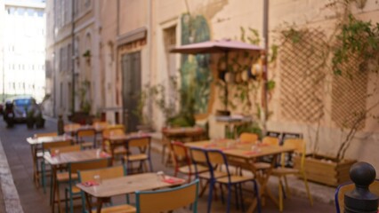 Outdoor cafe in marseilles, france, with blurred tables and chairs in a sunny street, featuring bokeh and defocused urban background, creating a serene atmosphere.