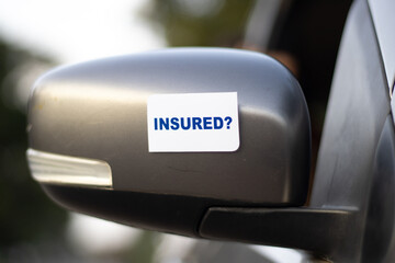 Insured? message sticked to the side mirror on a car to make awareness about Insurance