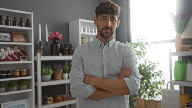 Handsome young man with arms crossed standing in a home decor store, surrounded by stylish interior decorations and plants