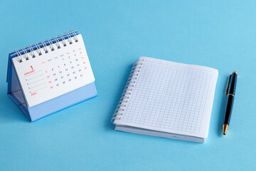 A desktop calendar for 2025, a ballpoint pen and an open notebook on a blue background. The planning concept.
