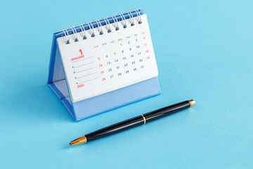 A desktop calendar for 2025 and a black ballpoint pen on a blue background.