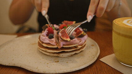 Woman at restaurant enjoying pancakes with fresh fruit topping coffee on table
