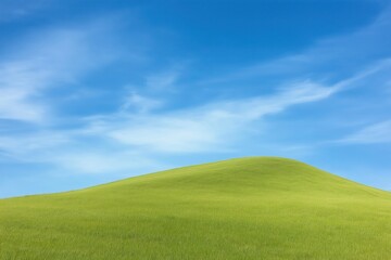 Rich green grassy hill slopes gently against clear vibrant blue sky dotted with wispy clouds. Perfect for nature scenery in rural park setting. Daylight fills scene. Beautiful natural colors. Ideal