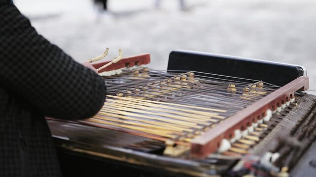 Street performer play traditional cymbal musical instrument with sticks over strings, slow motion