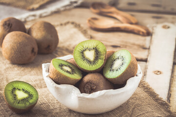 Whole and halfed kiwis in a white bowl on a rustic wooden table