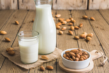 Glass and pitcher with vegan almond milk, almond kernels and whole almonds on an old rustic wooden table