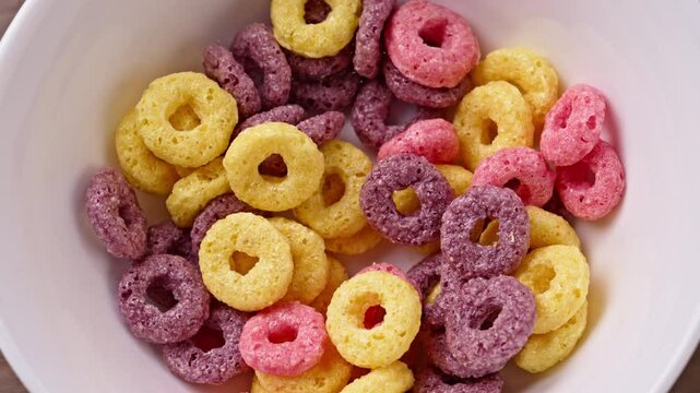 Close up of sugary flakes breakfast cereal with sweet fruit flavor falling effectively on white plate.