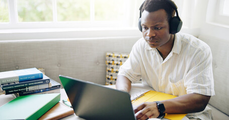 Black man, laptop and headphones with typing in home with studying, assessment or listening to music with scholarship. Person, student and computer with notes, education or elearning for college exam
