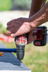 Installation work of a wooden gazebo, the master is screwing screws into the wooden floor.