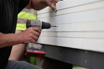 The builder attaches the wall to the gazebo frame using screws and a screwdriver.