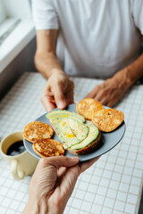 man has breakfast at home in kitchen. plate with avocado toast, pancakes and black coffee. bright and cozy place. healthy eating, vegetarian. top view of food. nutritious lunch, delicious balanced.