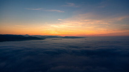 Capturing a stunning sunset casting a vibrant orange glow over a tranquil sea of clouds and rolling hills, creating a serene landscape