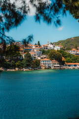 Obraz premium Whitewashed houses cluster on a hillside, overlooking a beautiful bay with crystal-clear turquoise water, framed by lush greenery under a vibrant blue sky