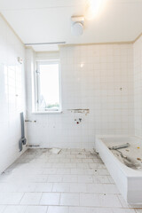 Bathroom undergoing renovation; tiles, plumbing, and tub are exposed.  Disarrayed debris is visible.