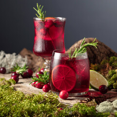 Cranberry cocktail with ice, lime, and rosemary on a old wooden board.