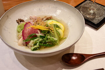 A light Japanese soup with fresh vegetables, radish slices, yellow squash, greens, chicken, and a clear broth, garnished with yuzu zest and sesame. Delicious and healthy dish.