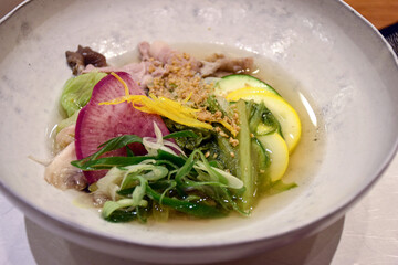 A light Japanese soup with fresh vegetables, radish slices, yellow squash, greens, chicken, and a clear broth, garnished with yuzu zest and sesame. Delicious and healthy dish.