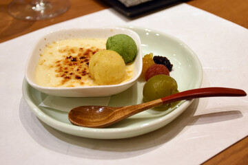 A creamy dessert topped with a caramelized sugar crust, accompanied by colorful scoops of ice cream and small sweet treats, served on a simple plate with a wooden spoon, reflecting Japanese elegance.