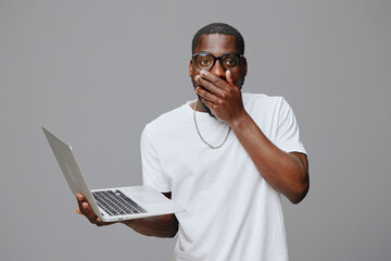 shocked man holding laptop, surprised expression, casual white t shirt, modern glasses, gray background, technology concept, emotional response to online news, digital communication