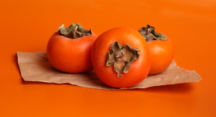 three persimmon fruits on orange background
