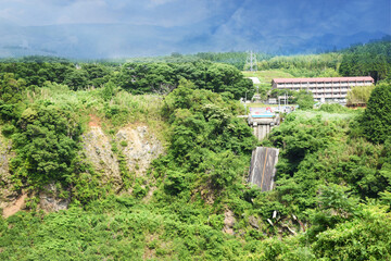 A collapsed road bridge surrounded by dense green vegetation (Sugaru Kuzure), Japan. Broken metal...